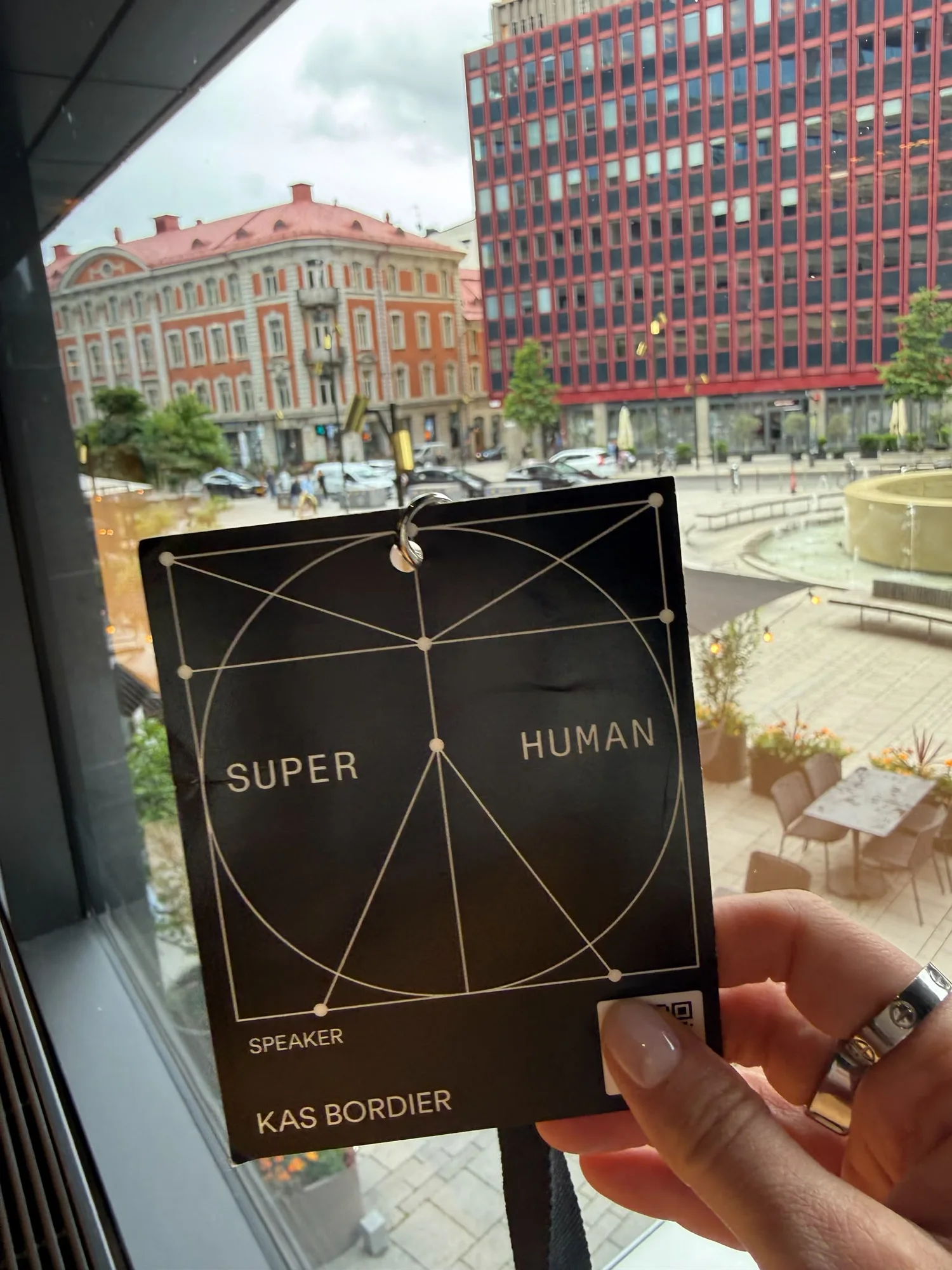 A black Super Human speaker pass reading Kas Bordier, held up against the square outside the venue in Stockholm