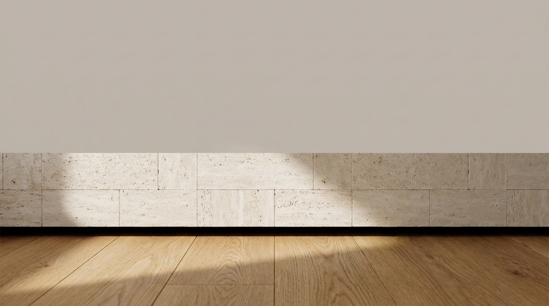 Raking light across a travertine skirting, lime plaster wall and wide oak boards
