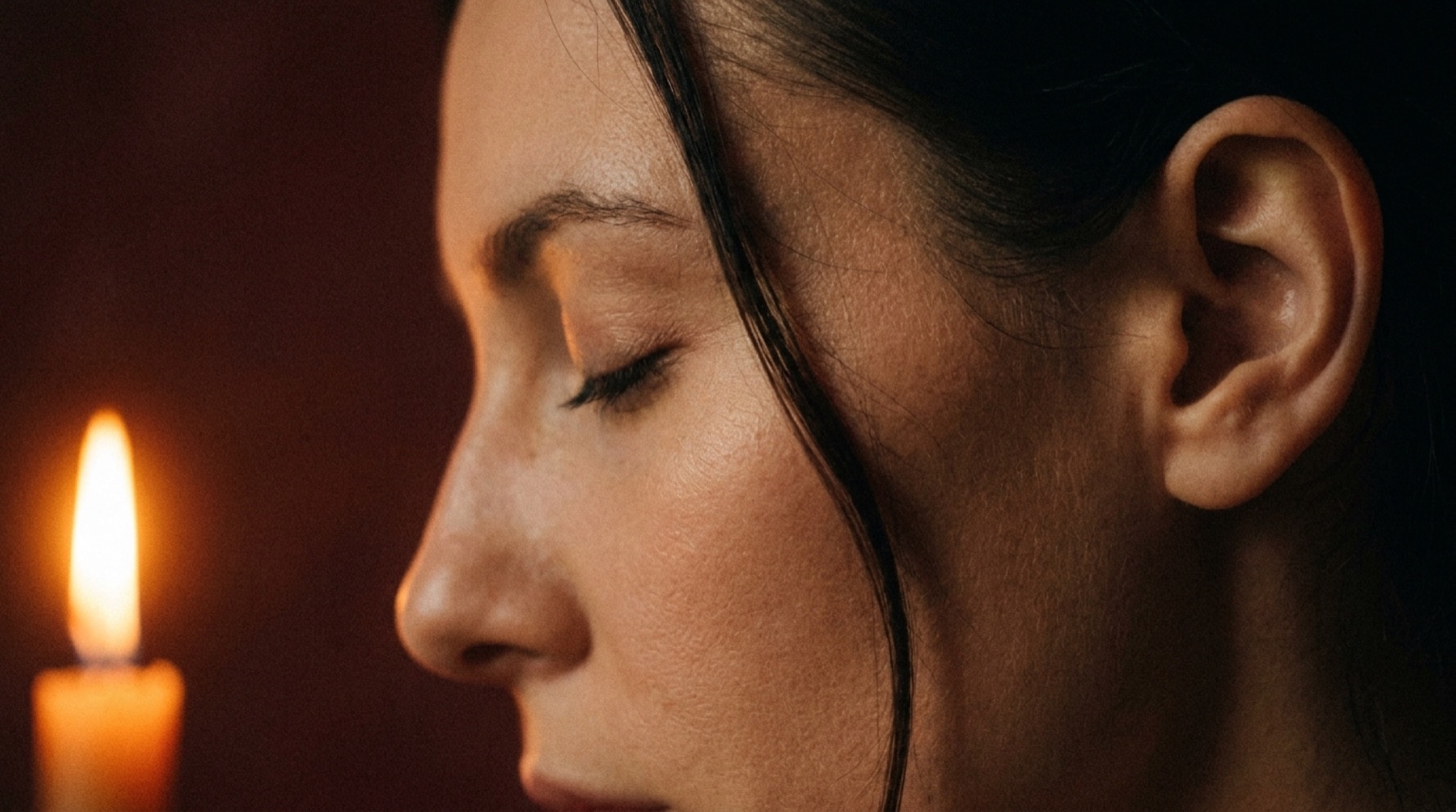 A woman's profile beside a candle flame against an oxblood plaster wall
